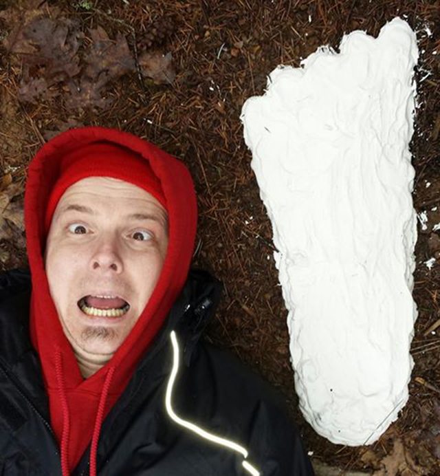 Johnny Manson poses next to a casting of a Sasquatch footprint.
