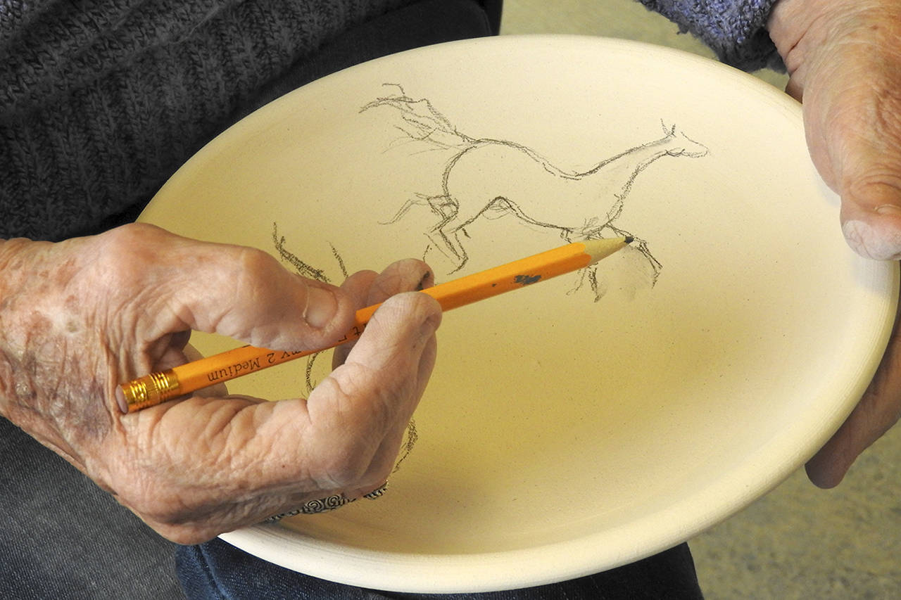 Guild member Ardith Forsgren draws a horse design to paint onto a bowl. (Kat Bryant | The Daily World)