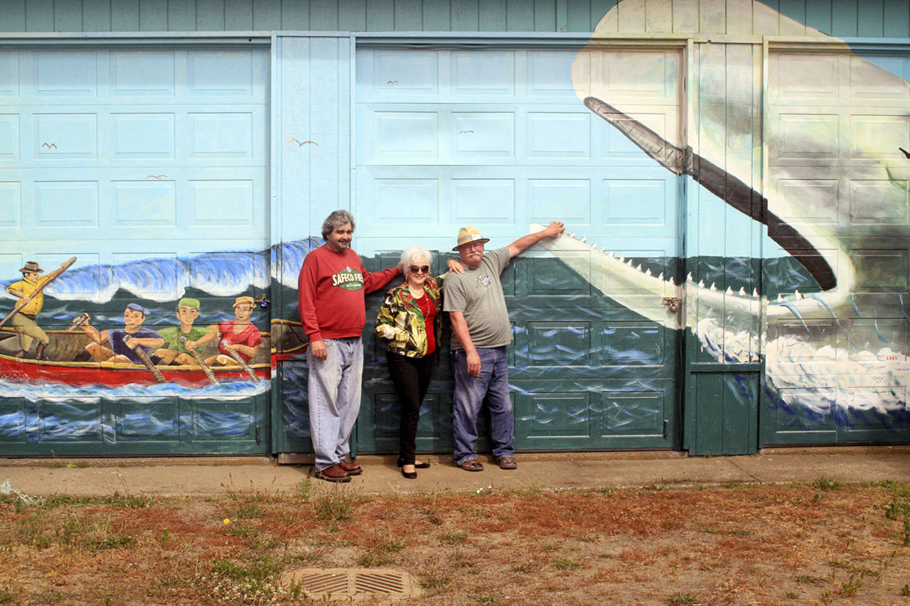 Members of Associated Arts of Ocean Shores, Joan Lohr, Jim Beauvais (wearing hat) and Michael Bedford donated their talent and time painting a massive mural next to Moby Dick restaurant on Pt. Brown Ave. in Ocean Shores. This is the second of 20 murals AAOS artists hope to paint in the area, with support from the community. Photo by Ed Schroll/AAOS