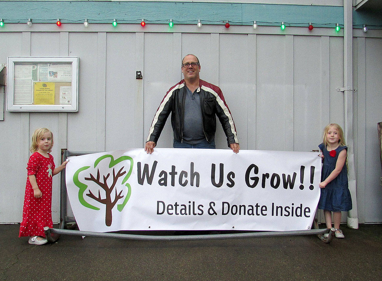 Scott D. Johnston photo: Frequent Ocean Shores Library users Scott Ennis and his daughters Susanna, 5, and Elena, 3, unveil the banner for the Library expansion campaign.