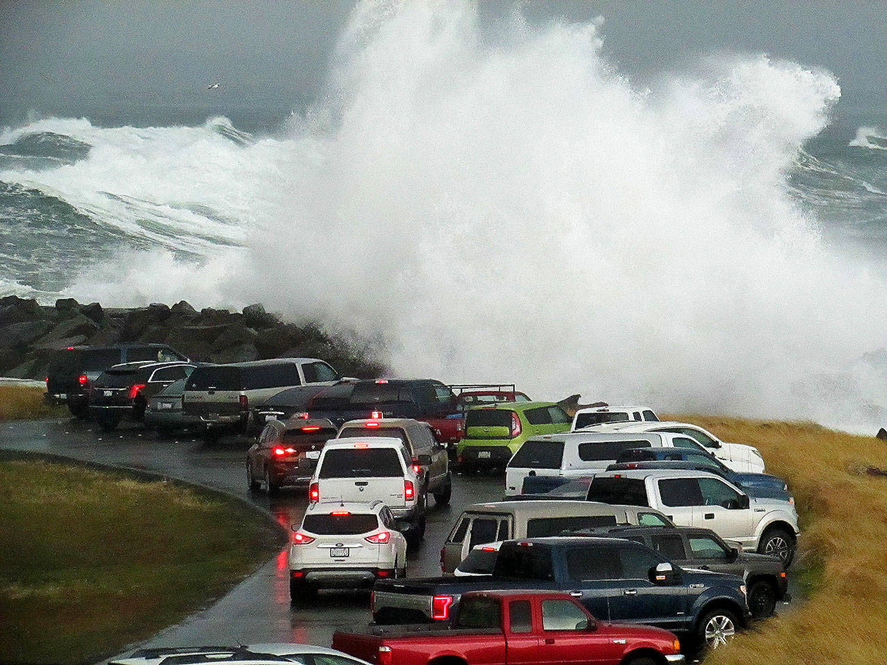 Scott D. Johnston photo: A wave breaks against the jetty rocks, sending spray onto the vehicles in the parking lot at the end of Ocean Shores Boulevard during the high surf storm surge at high tide on Thursday afternoon.