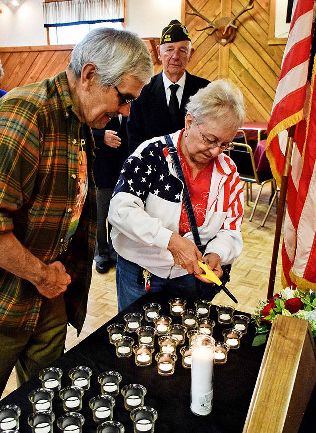 Army veteran Heinz Lemke looks on as Elks member Marti St. Germain lights a memorial candle, with VFW Post office Bob Howe in the background.